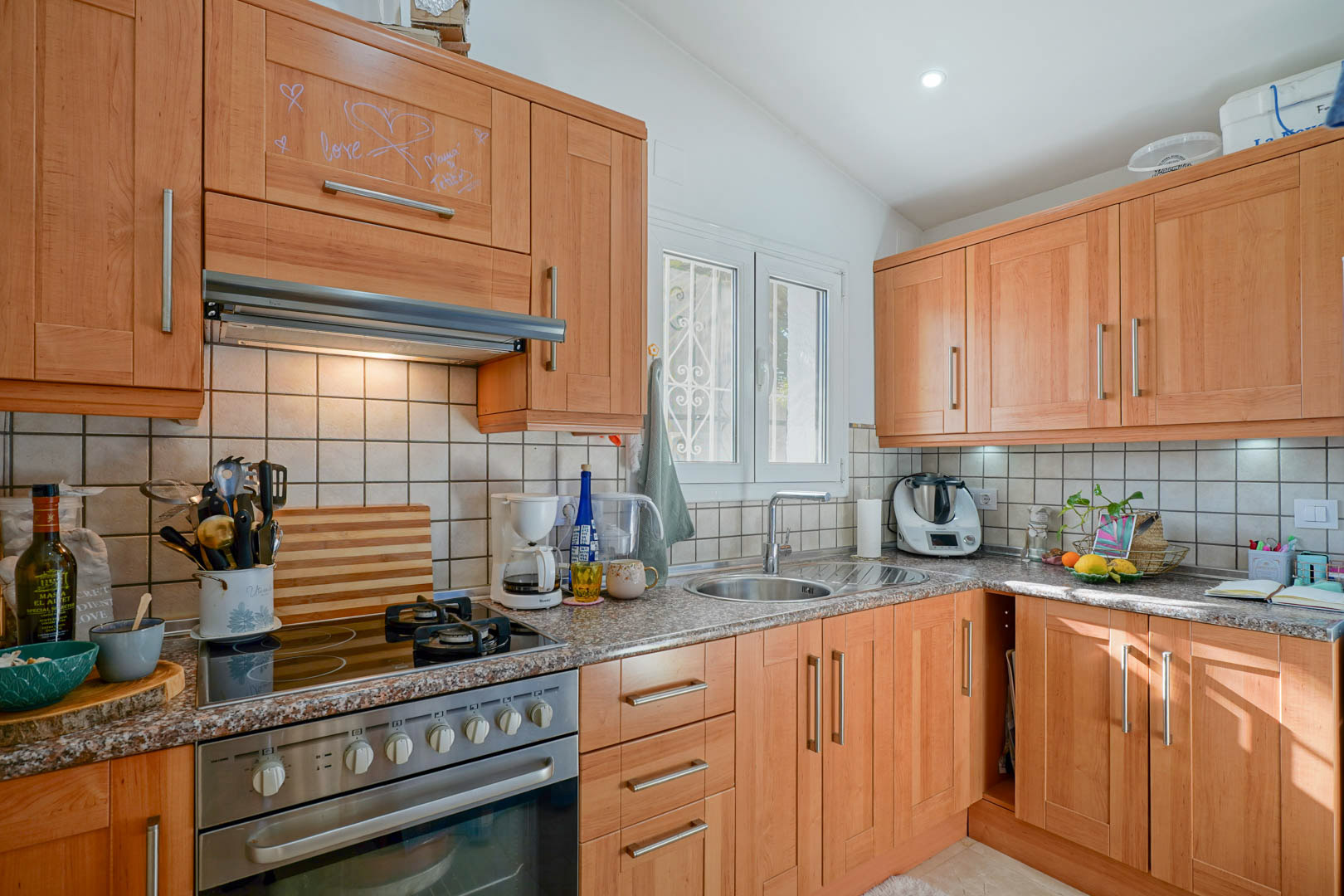 Cuisine indépendante avec meubles en bois, plan de travail en granit et plaque mixte. Elle dispose d'un évier circulaire en inox et d'une fenêtre apportant de la clarté.