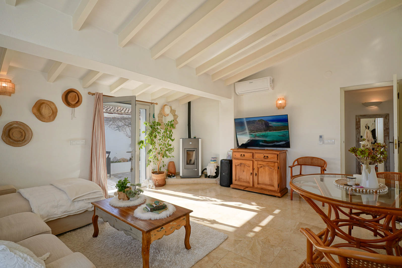 Salon-salle à manger avec plafonds à poutres apparentes blanches, poêle à granulés et sol en marbre. La pièce dispose de la climatisation et d'un accès à la terrasse.
