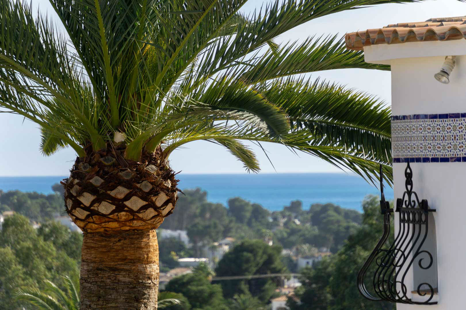 Vue sur la mer Méditerranée encadrée par un palmier et des détails architecturaux traditionnels, tels que des azulejos et de la ferronnerie.