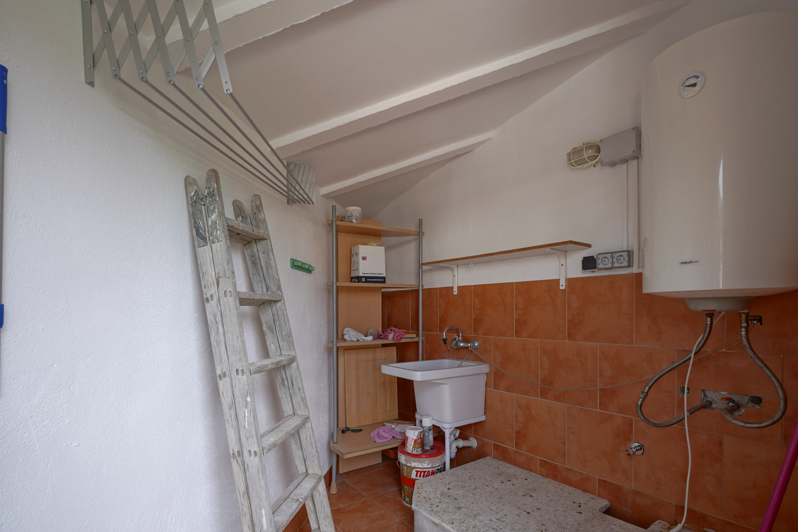 Buanderie et débarras fonctionnel avec plafond incliné, chauffe-eau électrique, évier de service et étendoir mural extensible.