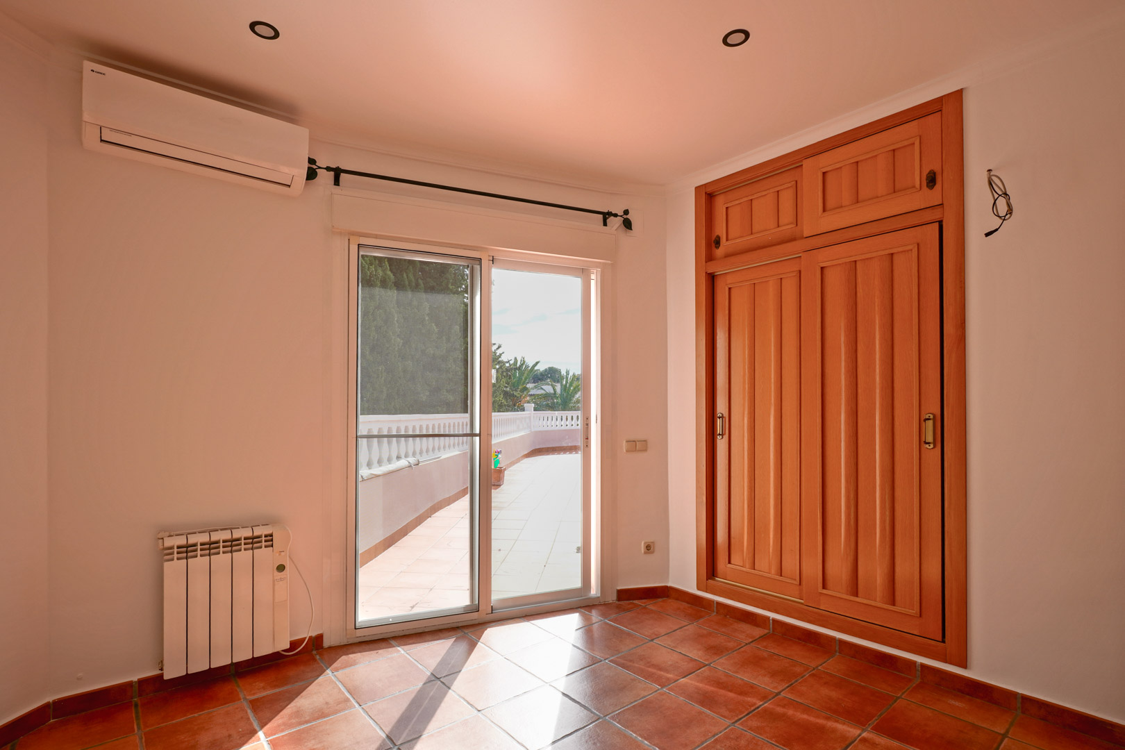 Chambre avec placard intégré en bois, sol en terre cuite et accès à la terrasse. Équipée d'une climatisation réversible, d'un radiateur électrique et de spots intégrés.