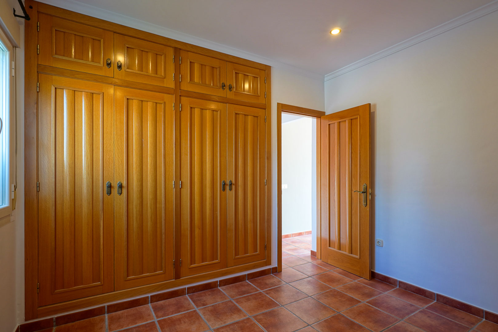 Chambre avec un grand placard intégré en bois du sol au plafond, sol en terre cuite traditionnelle et éclairage encastré au plafond.