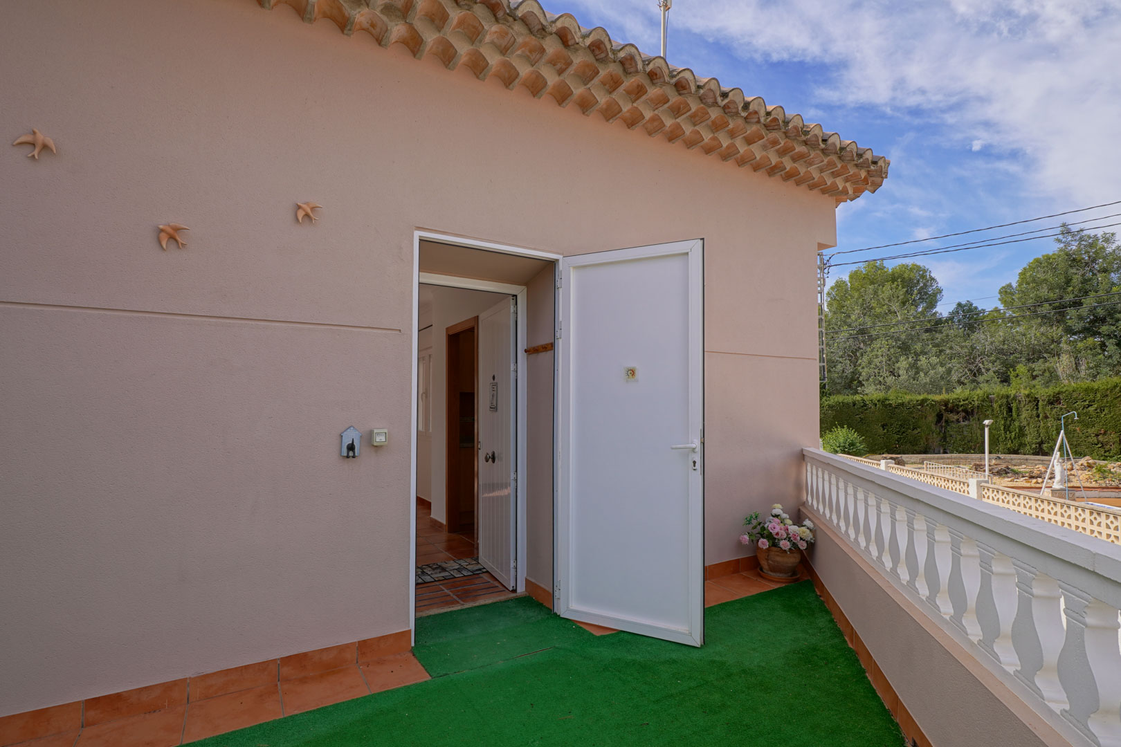 Entrée du penthouse depuis la terrasse supérieure, avec porte blanche, sol en terre cuite et balustrade classique donnant sur l'environnement naturel.