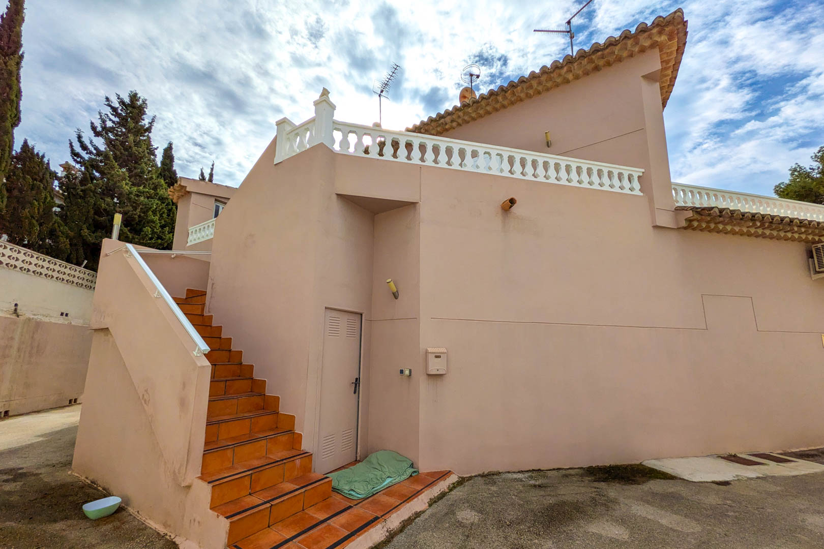 Escalier extérieur en grès cérame menant à l'étage supérieur, avec façade saumon et terrasse bordée d'une balustrade blanche traditionnelle.