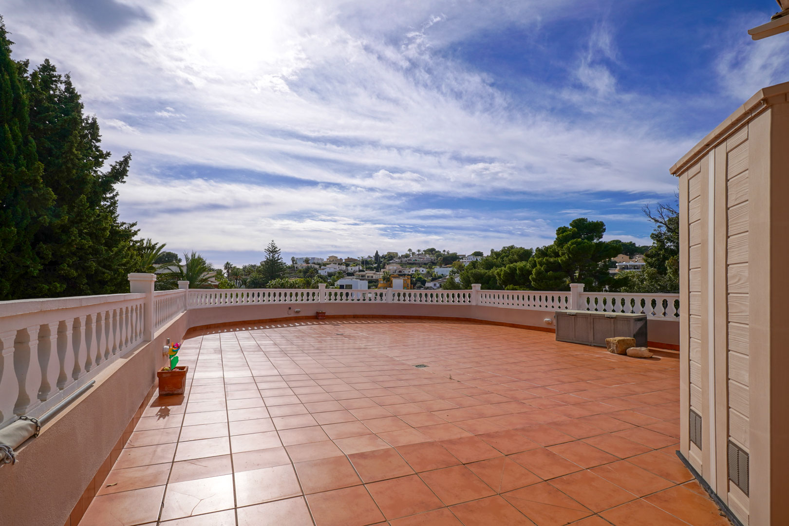 Grande terrasse extérieure avec revêtement en terre cuite et balustrade blanche, offrant une vue dégagée sur le paysage méditerranéen environnant.