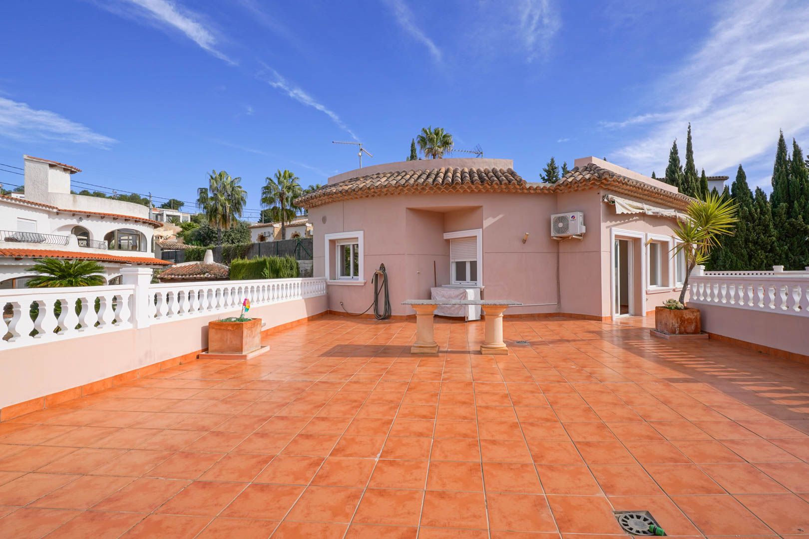 Grande terrasse sur le toit avec carrelage en terre cuite, balustrade blanche et table en pierre, offrant un espace extérieur dégagé.
