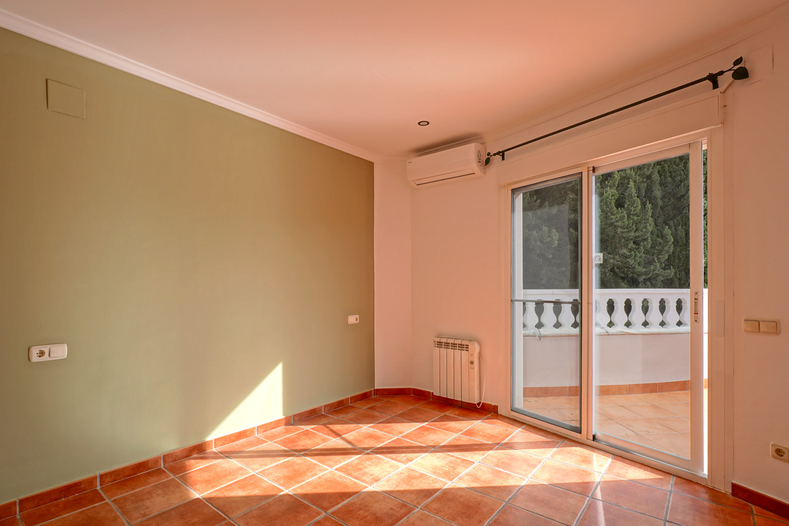 Pièce lumineuse avec mur vert, sol en terre cuite et accès terrasse. Comprend un climatiseur split, un radiateur électrique et des finitions soignées.