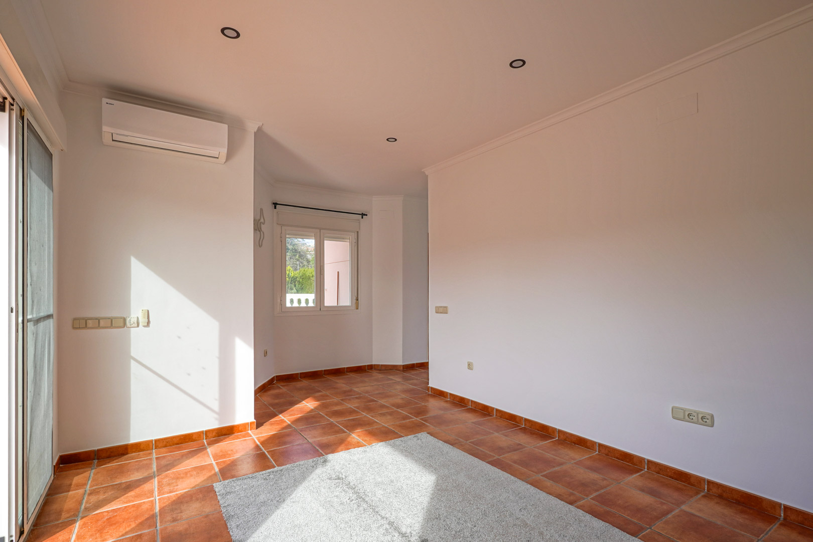 Salon-salle à manger lumineux avec sol en terre cuite rustique, climatisation réversible et accès direct à la terrasse par une baie vitrée.