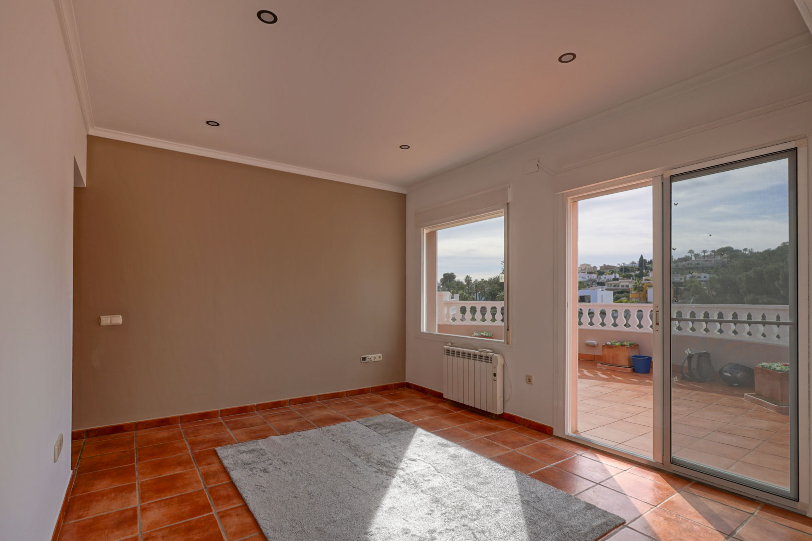 Séjour avec sol en terre cuite, éclairage encastré et accès direct à une grande terrasse. La pièce dispose d'un radiateur électrique et d'un mur d'accent.