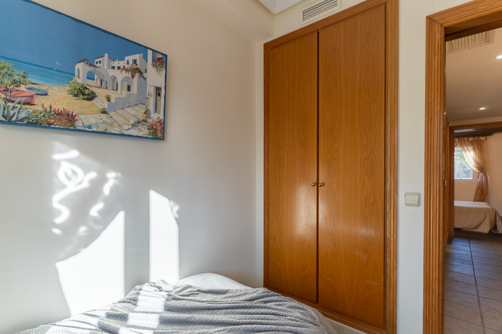 Chambre avec placard intégré en bois et lumière naturelle. L'ouverture mène à un couloir carrelé distribuant les différentes pièces de l'étage.
