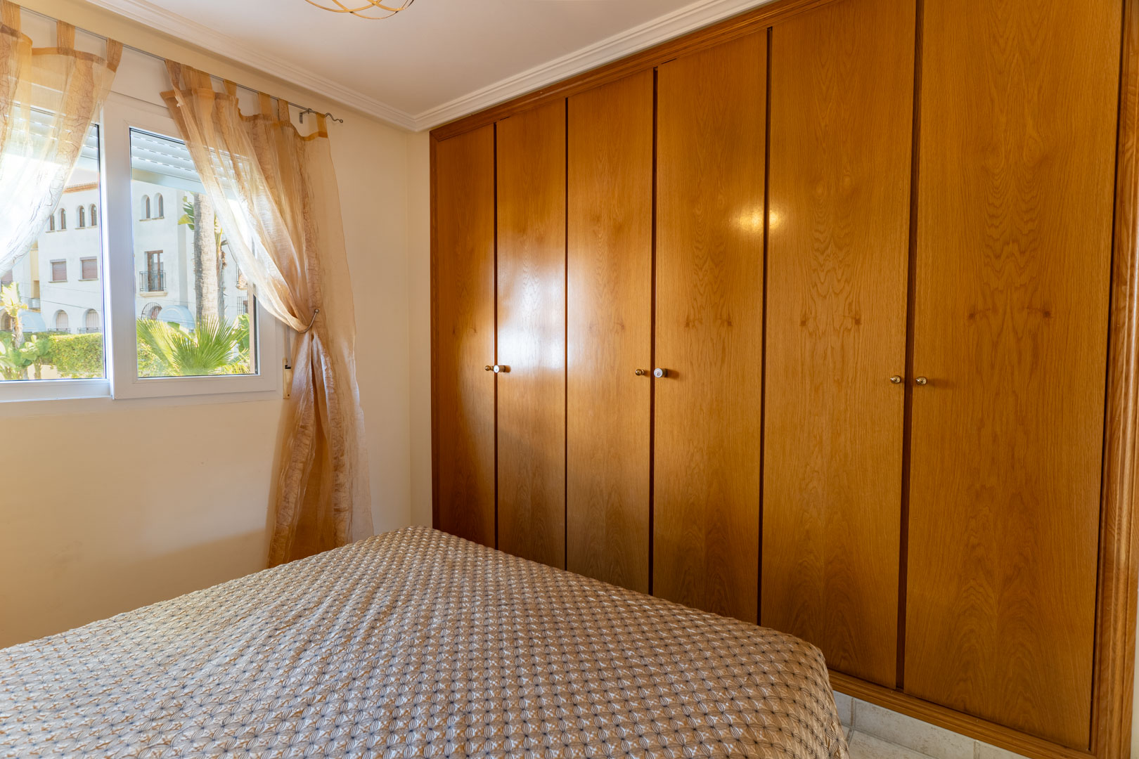 Chambre avec une grande armoire encastrée en bois à six portes et une fenêtre donnant sur les jardins extérieurs, offrant luminosité et rangement.