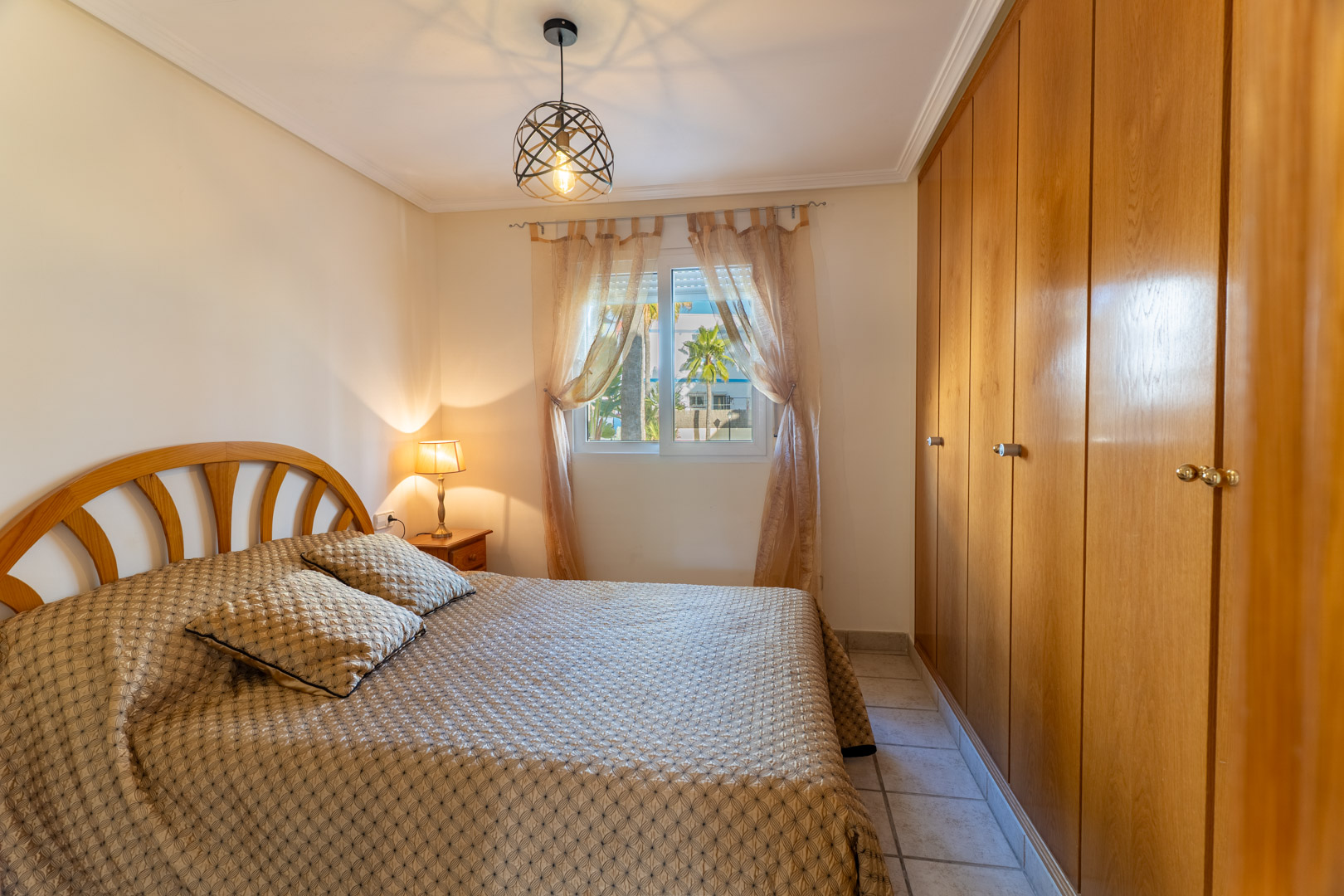 Chambre lumineuse avec de grands placards intégrés en bois, un lit double et une fenêtre offrant une vue sur les jardins de la résidence.