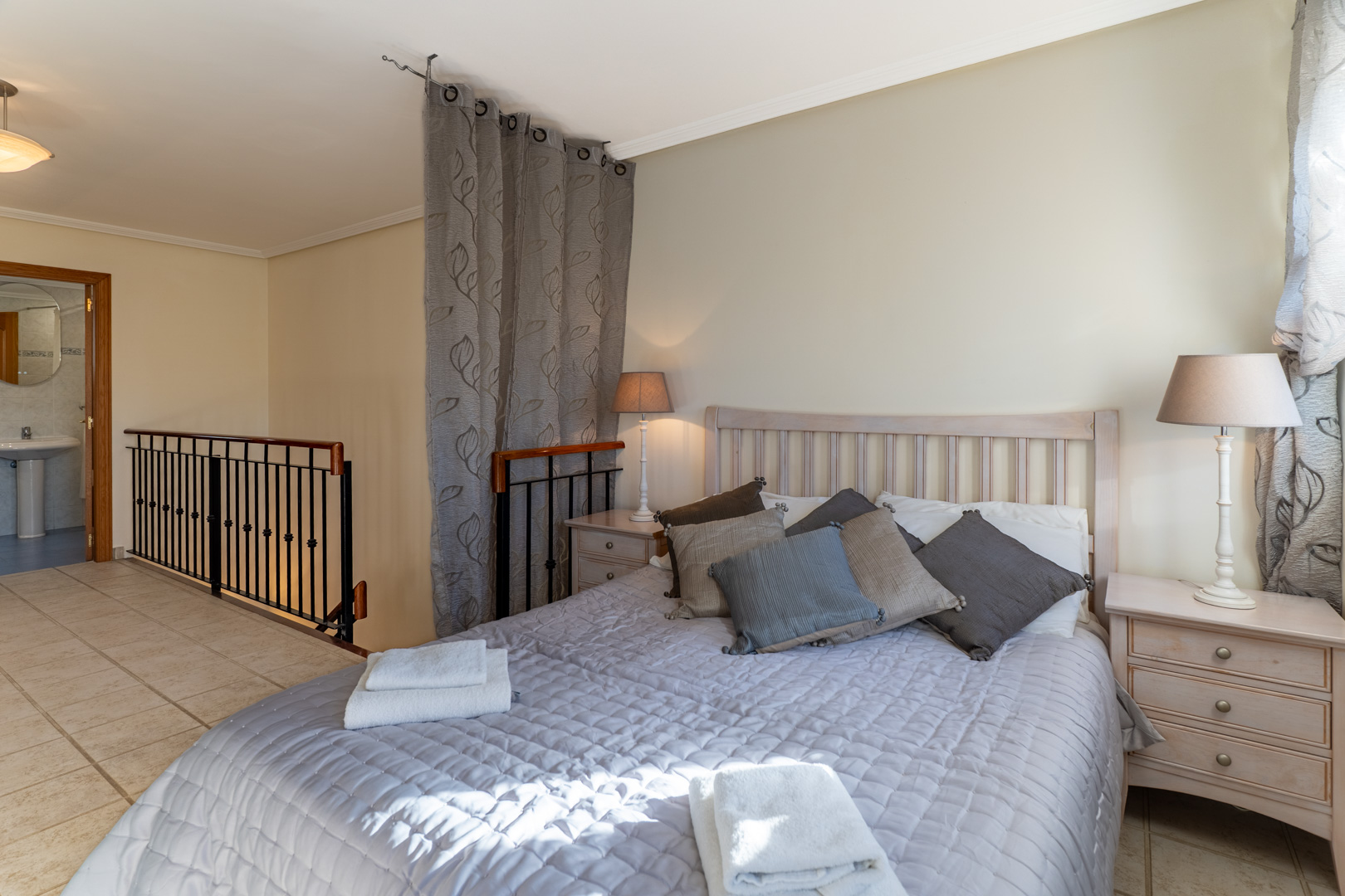 Chambre principale au dernier étage avec salle de bain attenante, sol en grès et rampe d'escalier en fer forgé noir.
