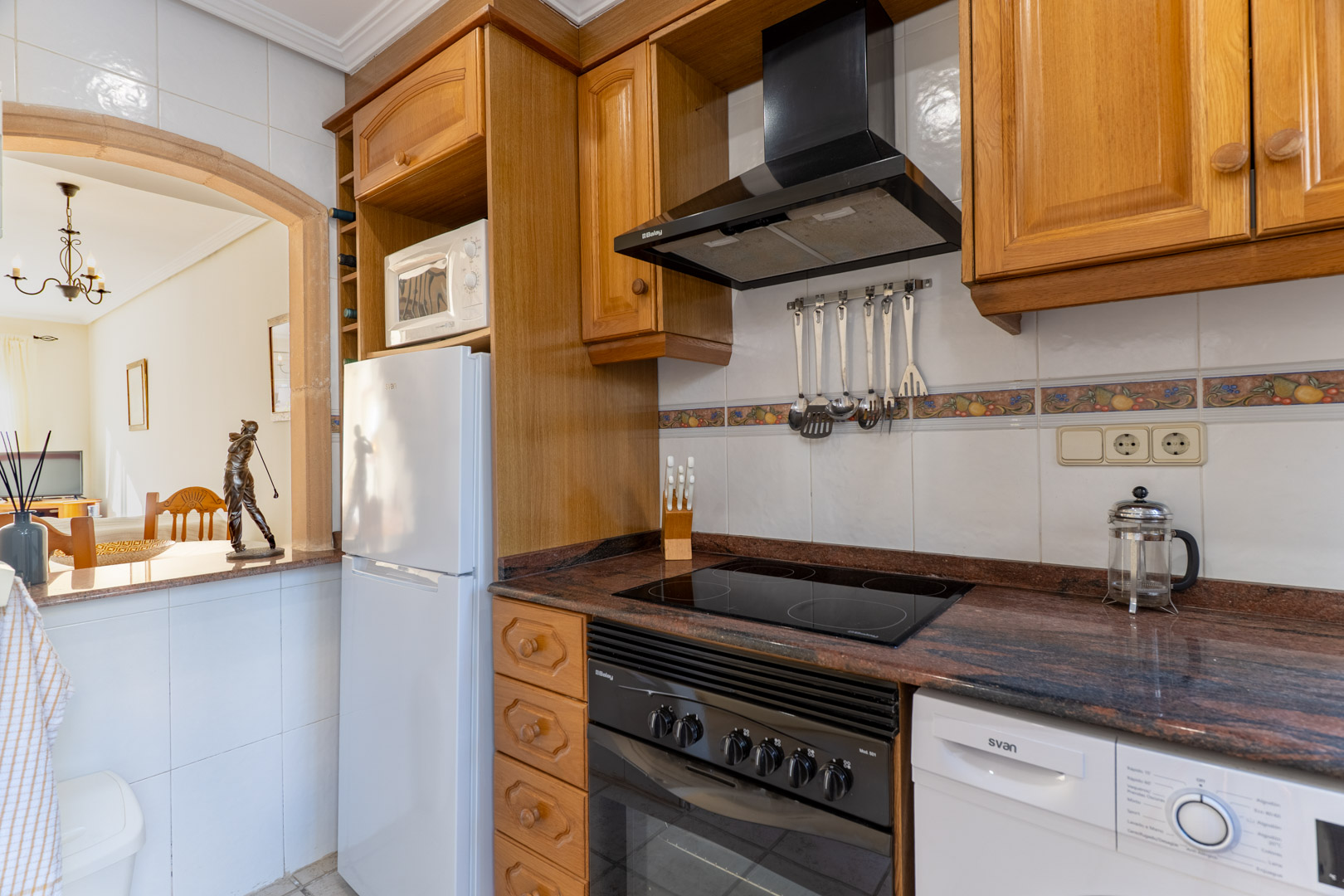 Cuisine fonctionnelle avec meubles en bois, plan de travail en granit et une arche décorative s'ouvrant sur la pièce de vie lumineuse.