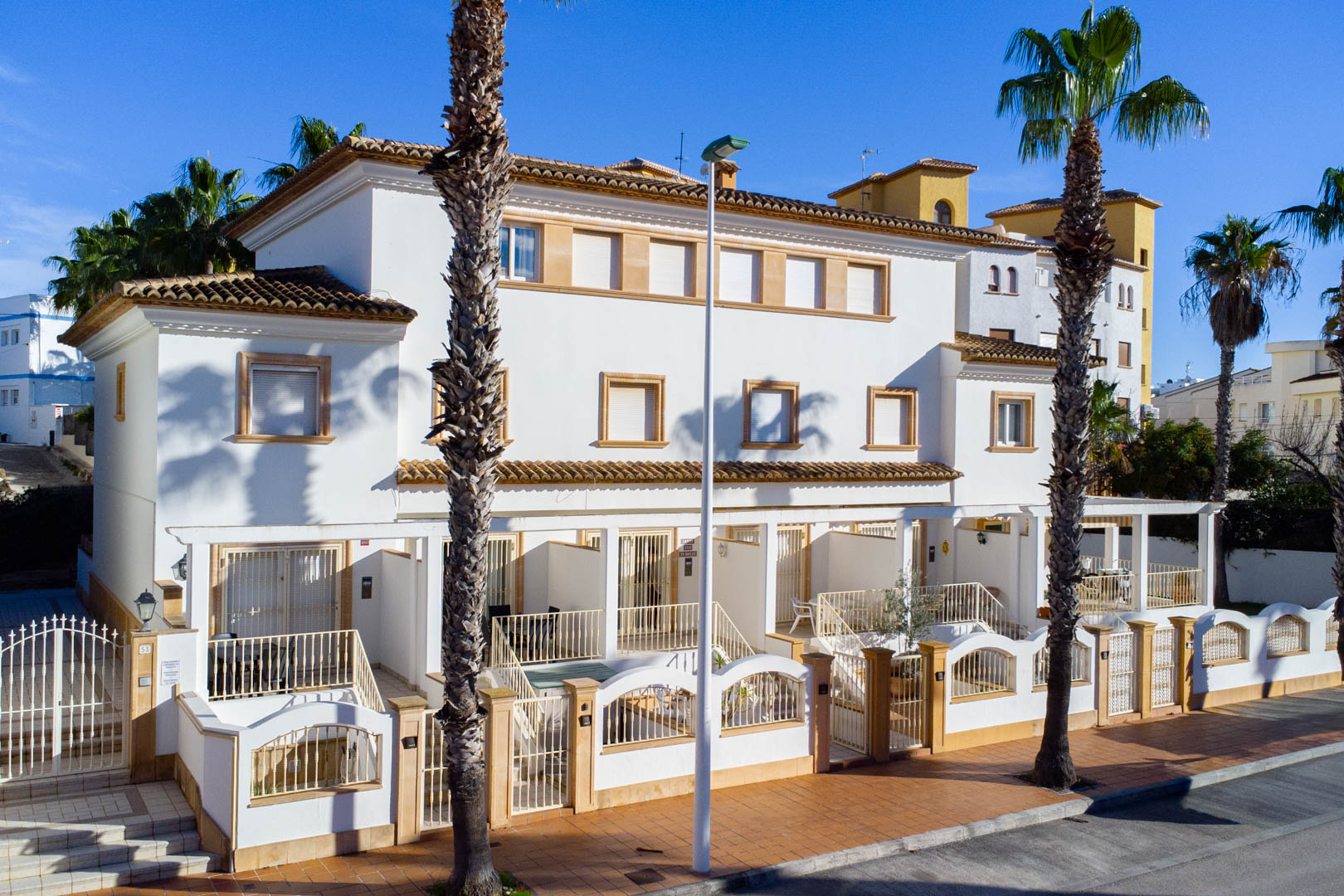 Façade extérieure de maisons de ville triplex de style méditerranéen avec murs blancs, encadrements en pierre et terrasses avant privées clôturées.