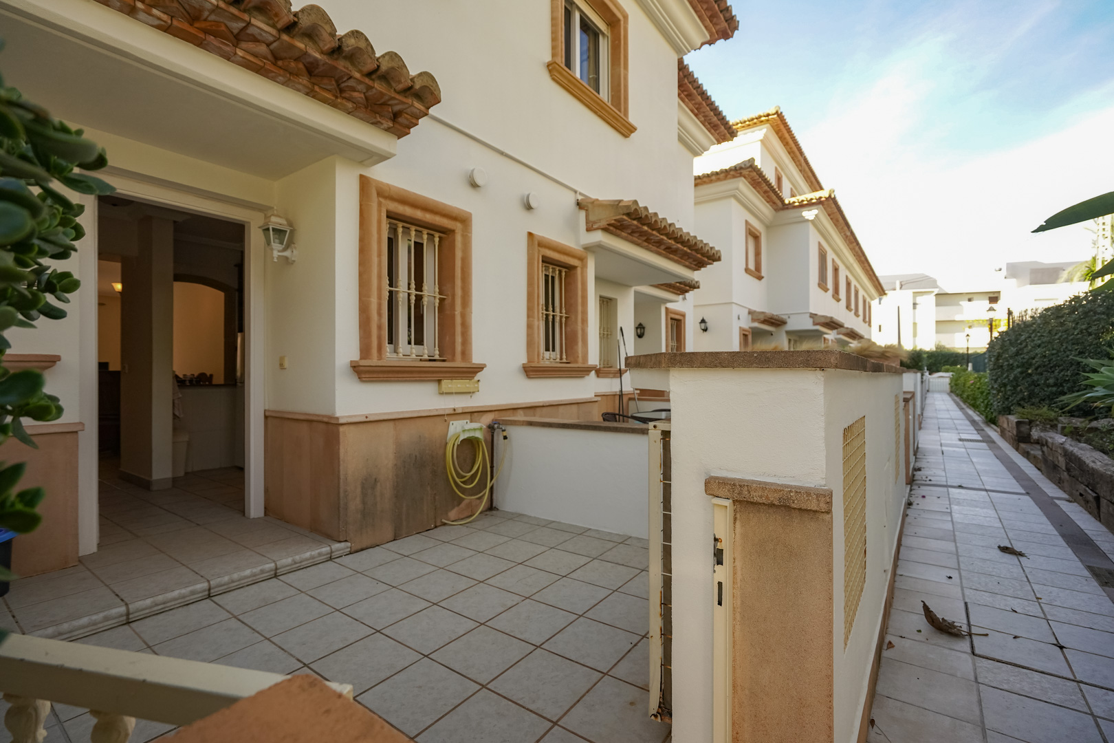 Façade extérieure du triplex avec terrasse avant carrelée, encadrements de fenêtres en pierre de Tosca et accès direct par l'allée piétonne de la résidence.