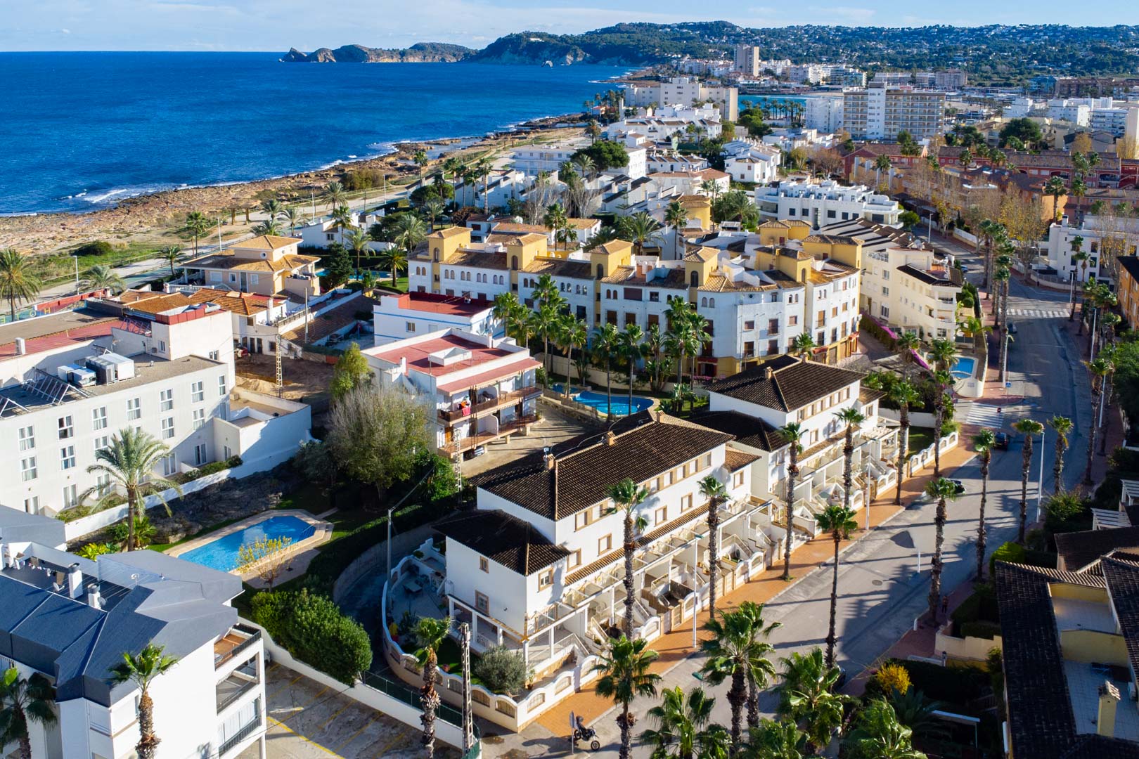 Vue aérienne du complexe Calle Génova, illustrant sa proximité avec la mer Méditerranée, la piscine communautaire et l'architecture aux façades blanches et palmiers.