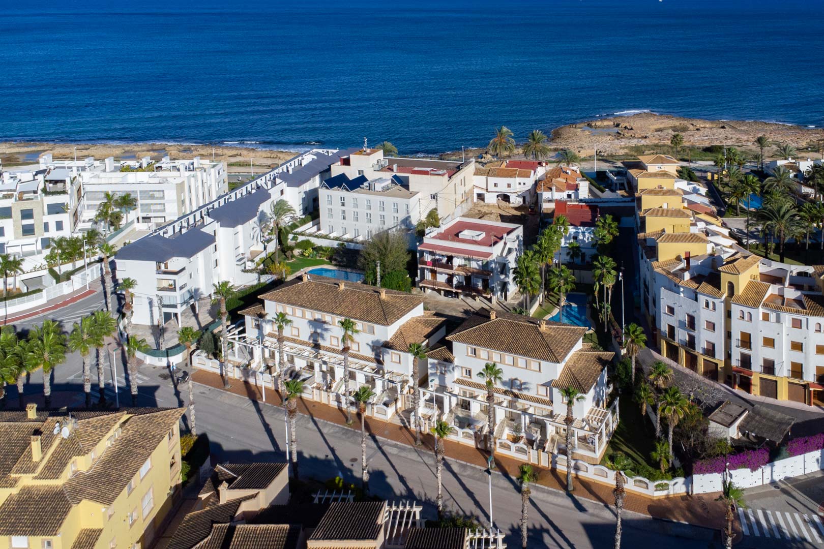 Vue aérienne du complexe Calle Génova, soulignant sa proximité avec la mer Méditerranée et l'architecture aux façades blanches et toits de tuiles bordés de palmiers.