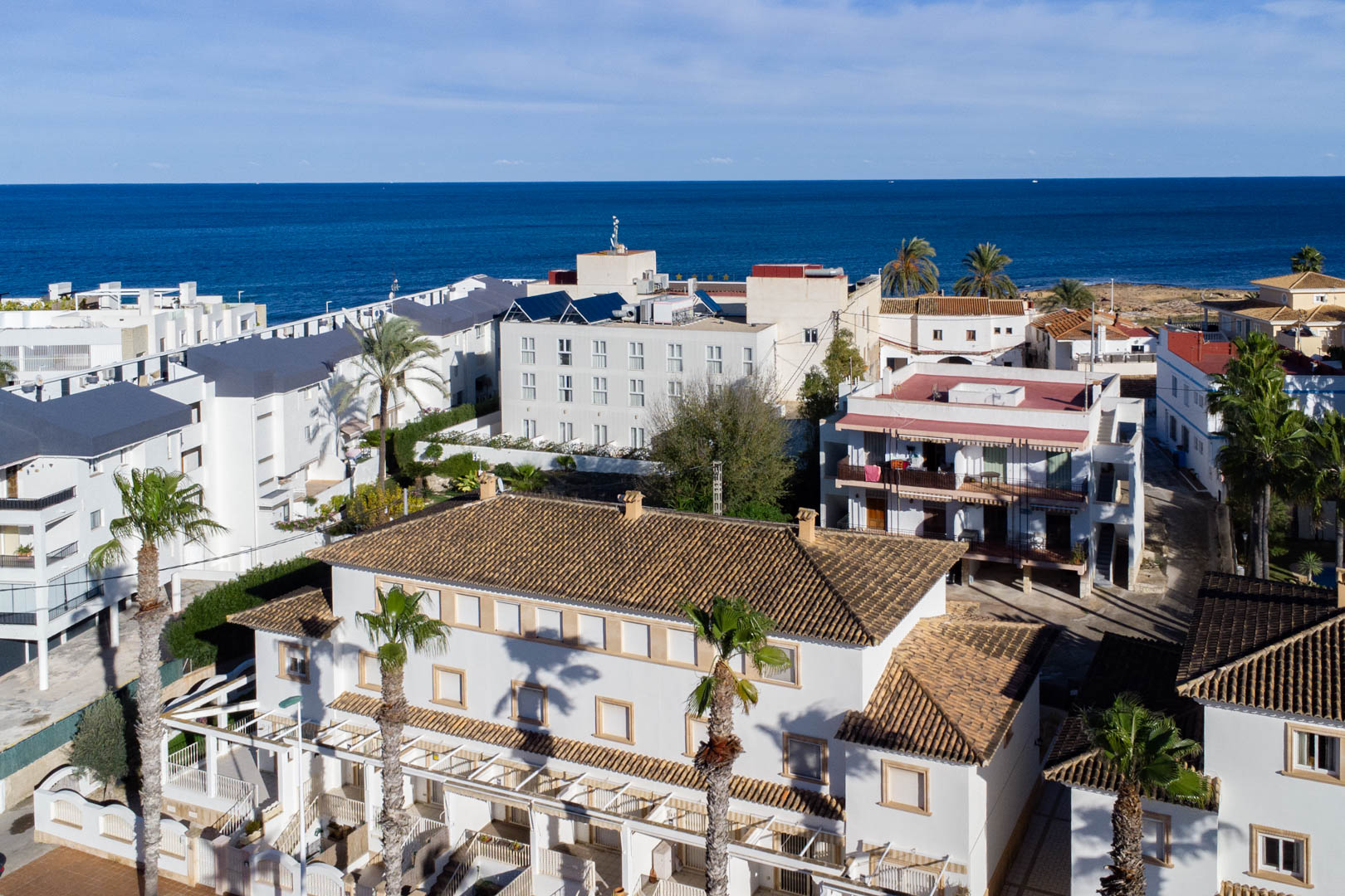 Vue aérienne du complexe résidentiel avec toits en tuiles et façades blanches, illustrant sa proximité immédiate avec la mer Méditerranée et les palmiers.