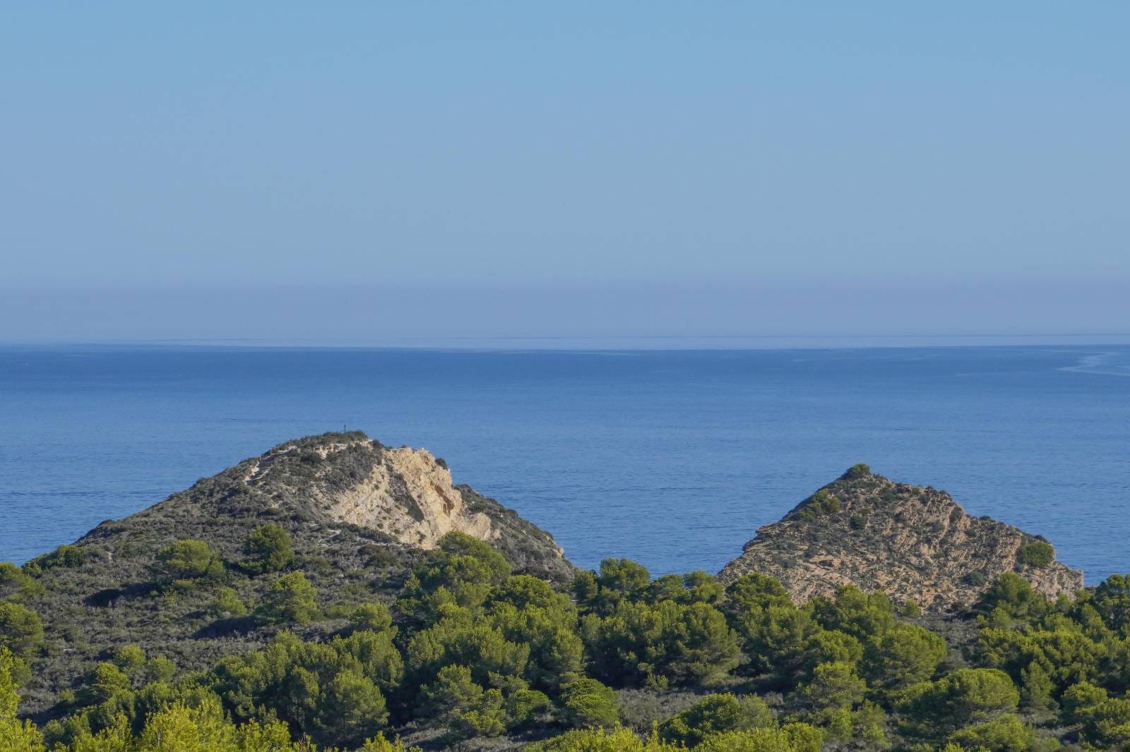 Vue panoramique sur la mer Méditerranée, mettant en valeur les collines rocheuses et les pinèdes verdoyantes typiques du littoral de Jávea.