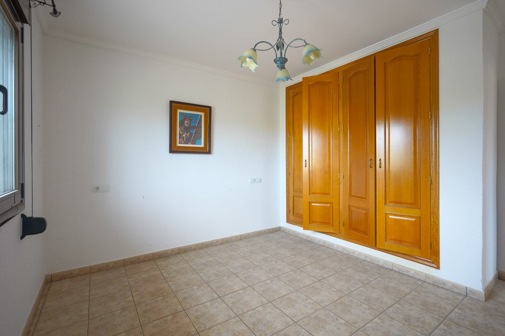 Pièce vide avec une grande armoire encastrée en bois à quatre portes, un sol en carrelage céramique beige et un lustre décoratif aux abat-jours en forme de fleurs.