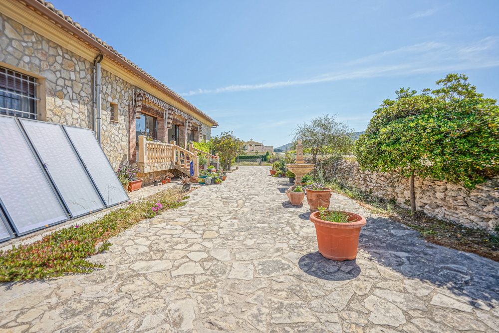 Terrasse extérieure en pierre naturelle avec fontaine, pots en terre cuite et panneaux solaires thermiques installés contre la façade en maçonnerie.