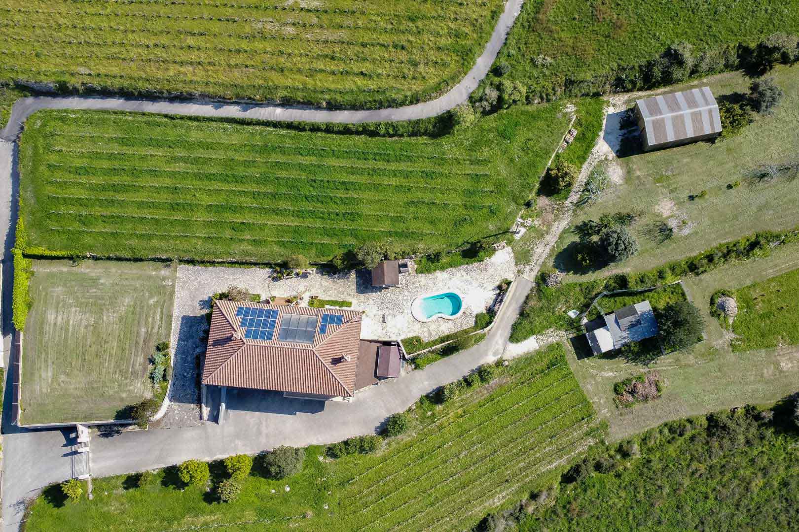 Vue aérienne d'une propriété rurale avec panneaux solaires, piscine de forme libre et vastes terrains agricoles structurés en rangées de cultures.