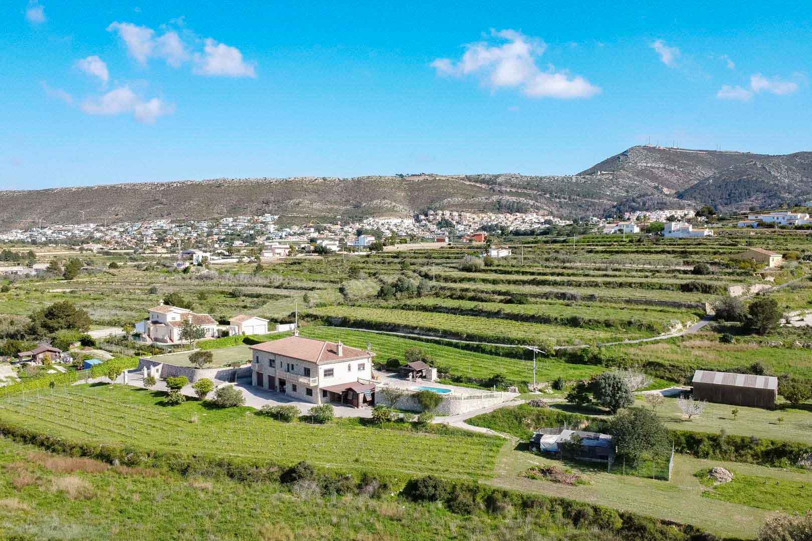 Vue aérienne d'une résidence en pierre à deux niveaux avec piscine, située sur un terrain agricole en terrasses face aux montagnes.