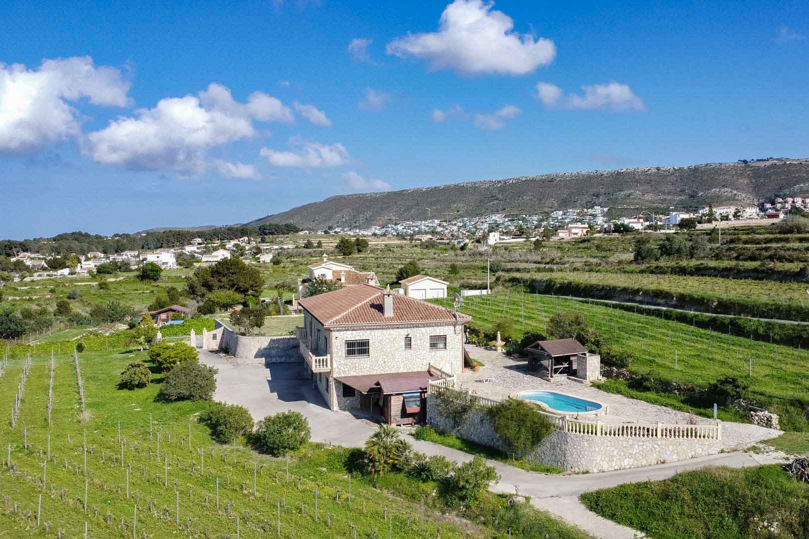 Vue aérienne d'une villa en pierre avec piscine, terrasse à balustrades et vastes vignobles, située dans un environnement rural avec vue sur les collines.