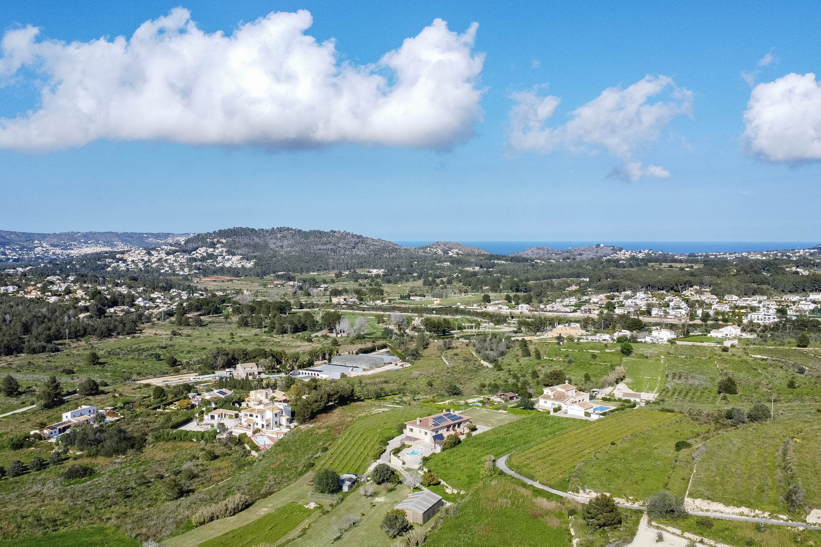 Vue aérienne panoramique du paysage méditerranéen, révélant des vallées verdoyantes, des villas avec piscines et l'horizon marin au loin.