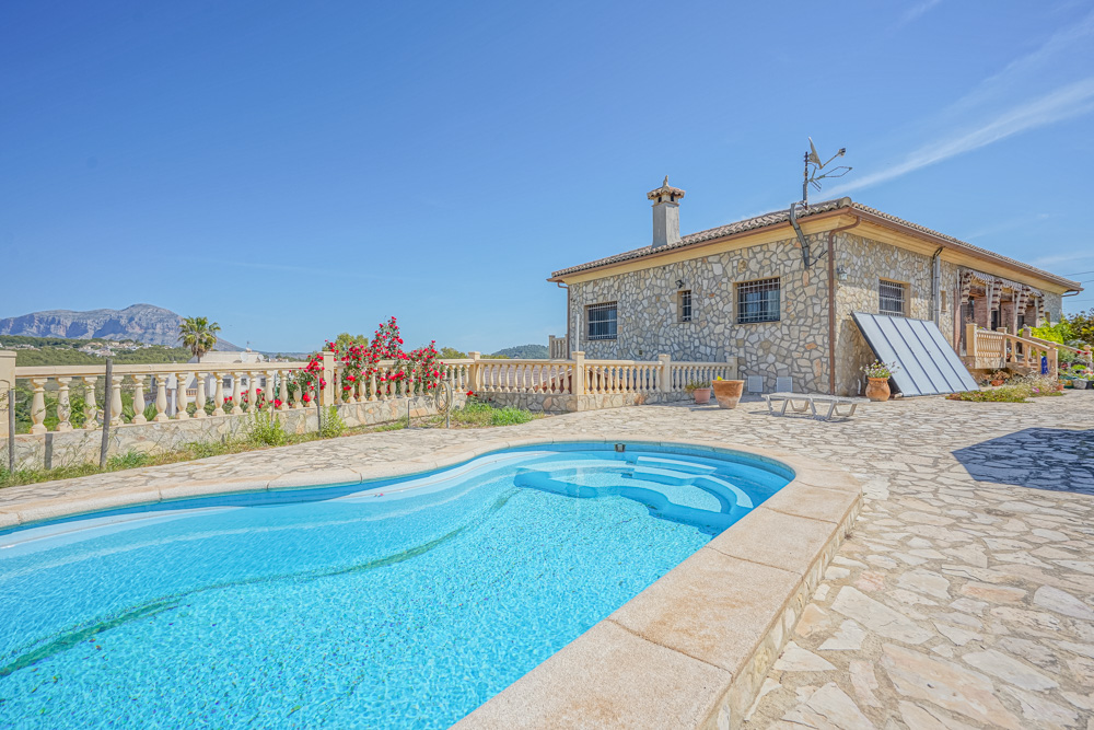Vue extérieure comprenant une piscine incurvée et une villa en pierre. La terrasse pavée de dalles irrégulières offre une vue panoramique sur les montagnes.