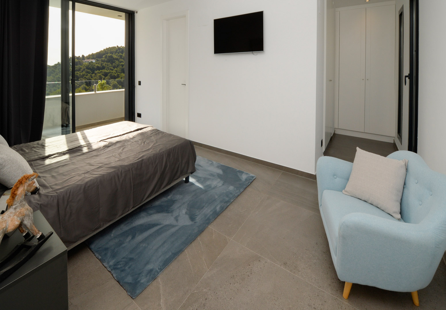 Chambre contemporaine avec accès terrasse, sol en grès gris, placards intégrés blancs et vue panoramique sur les collines verdoyantes.