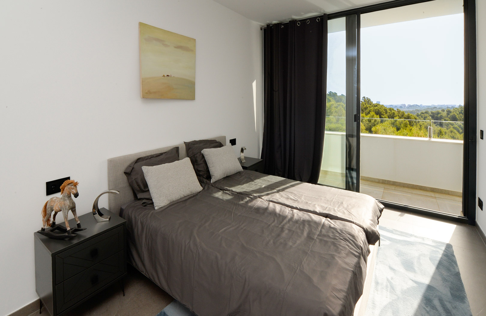 Chambre lumineuse avec lit double, tables de chevet minimalistes et grande baie vitrée offrant un accès direct à la terrasse avec vue sur les collines verdoyantes.