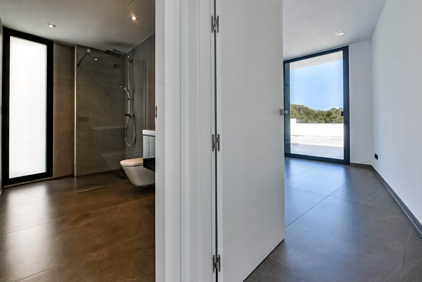 Chambre principale avec salle de bain attenante, douche à l'italienne, carrelage grand format et accès direct à la terrasse par de larges baies vitrées.