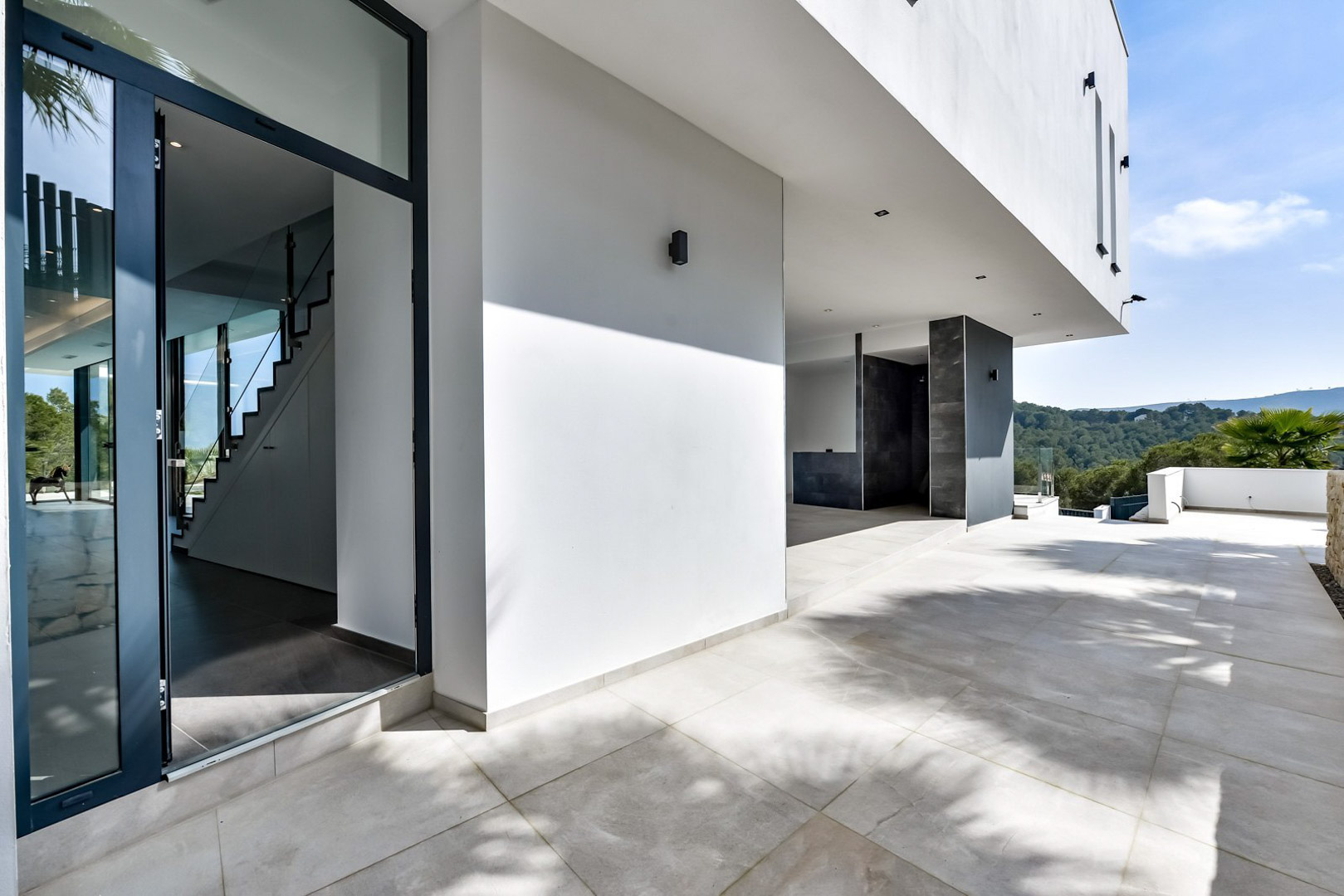 Entrée principale et terrasse couverte avec sol en grès cérame, architecture blanche minimaliste et vue dégagée sur la vallée de Jávea.