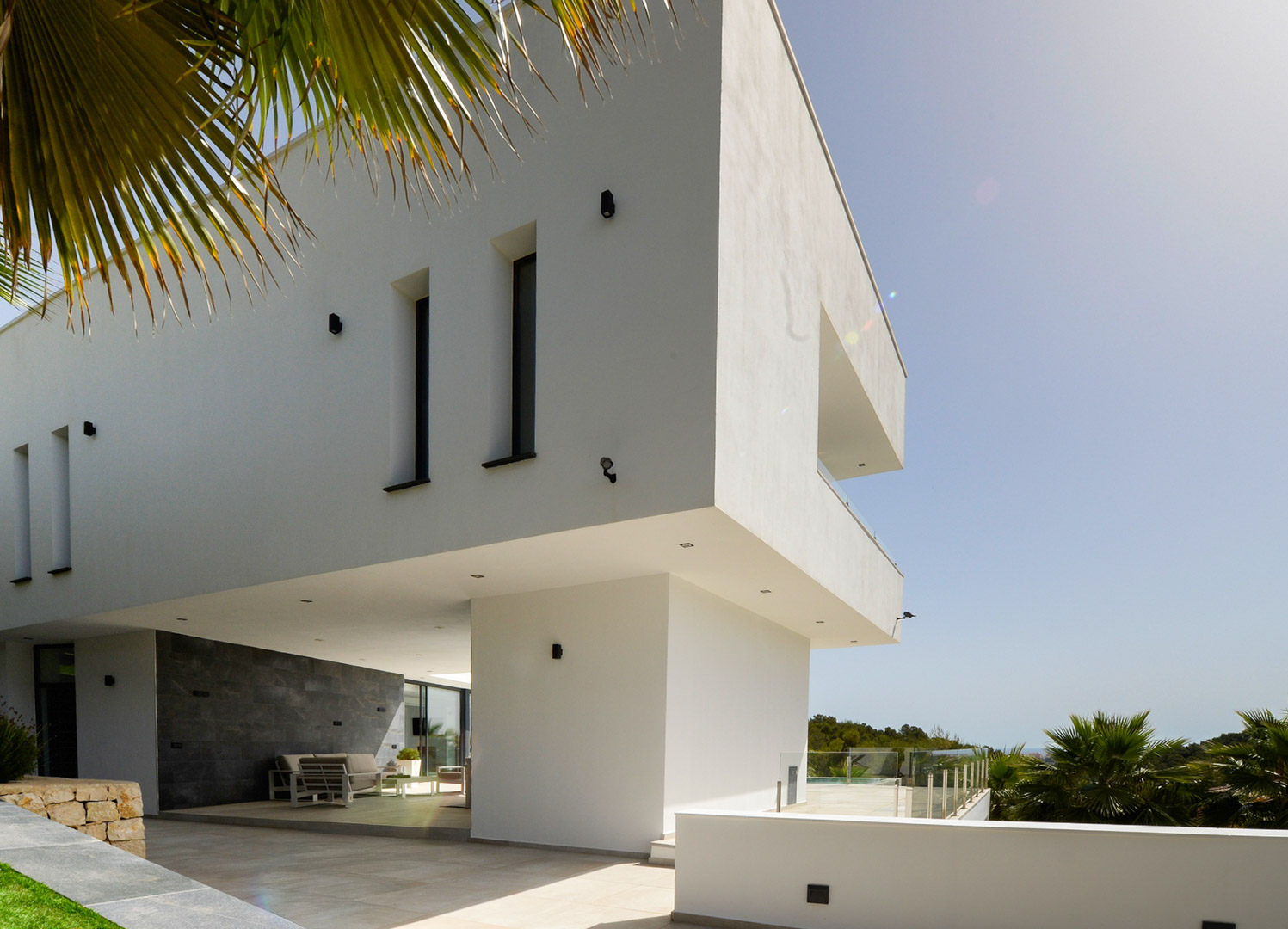 Façade contemporaine avec porte-à-faux architectural, murs en pierre naturelle grise et terrasse couverte avec mobilier d'extérieur et éclairage encastré.