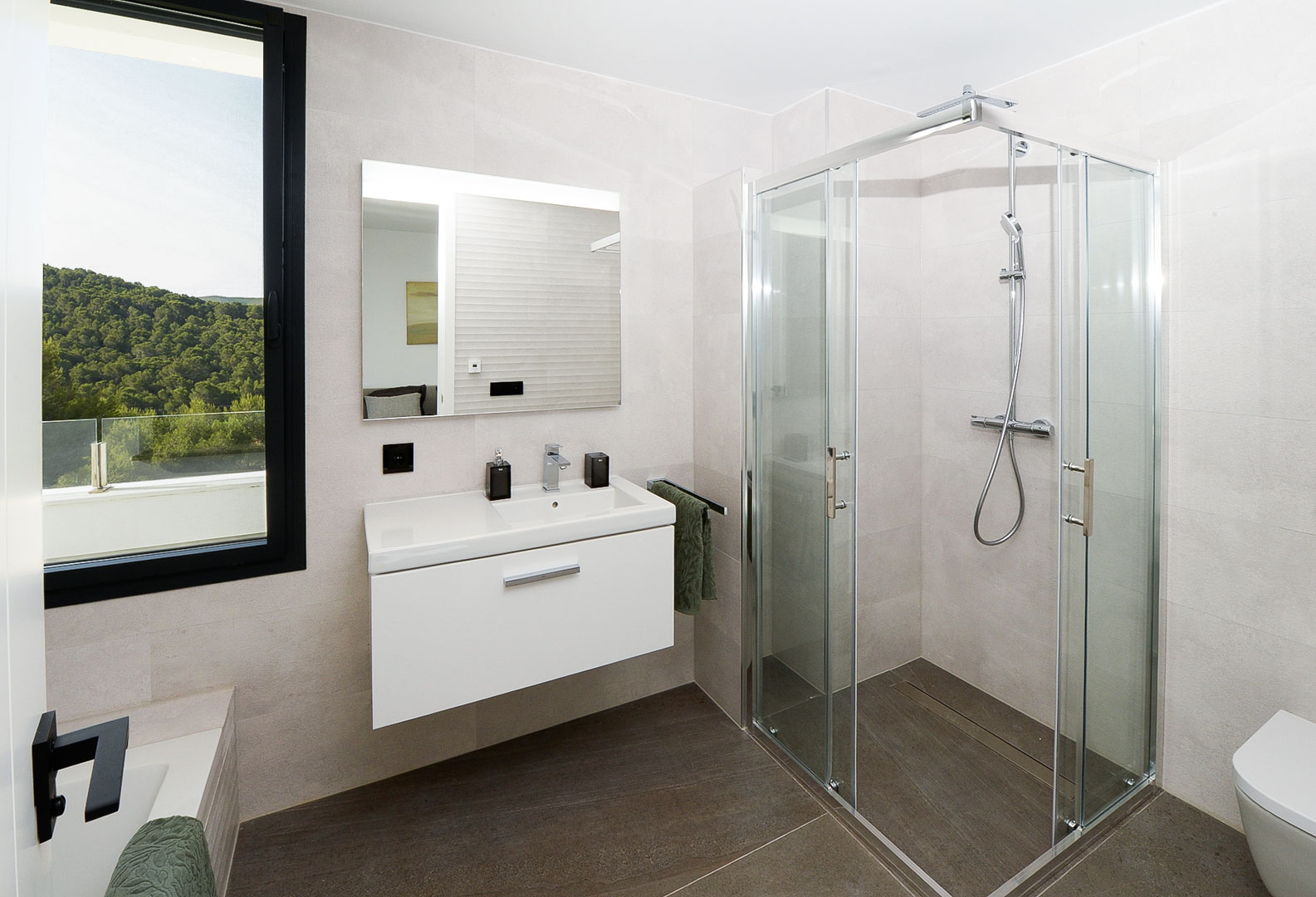 Salle de bain moderne avec cabine de douche en verre, meuble vasque suspendu blanc et fenêtre offrant une vue sur les collines verdoyantes.