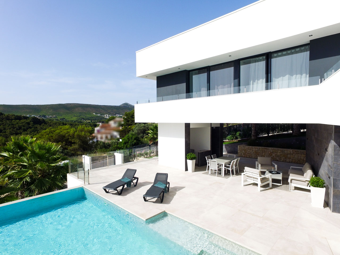 Terrasse principale avec piscine à débordement, chaises longues et salon d'été abrité sous l'étage supérieur, offrant une vue dégagée sur la nature.