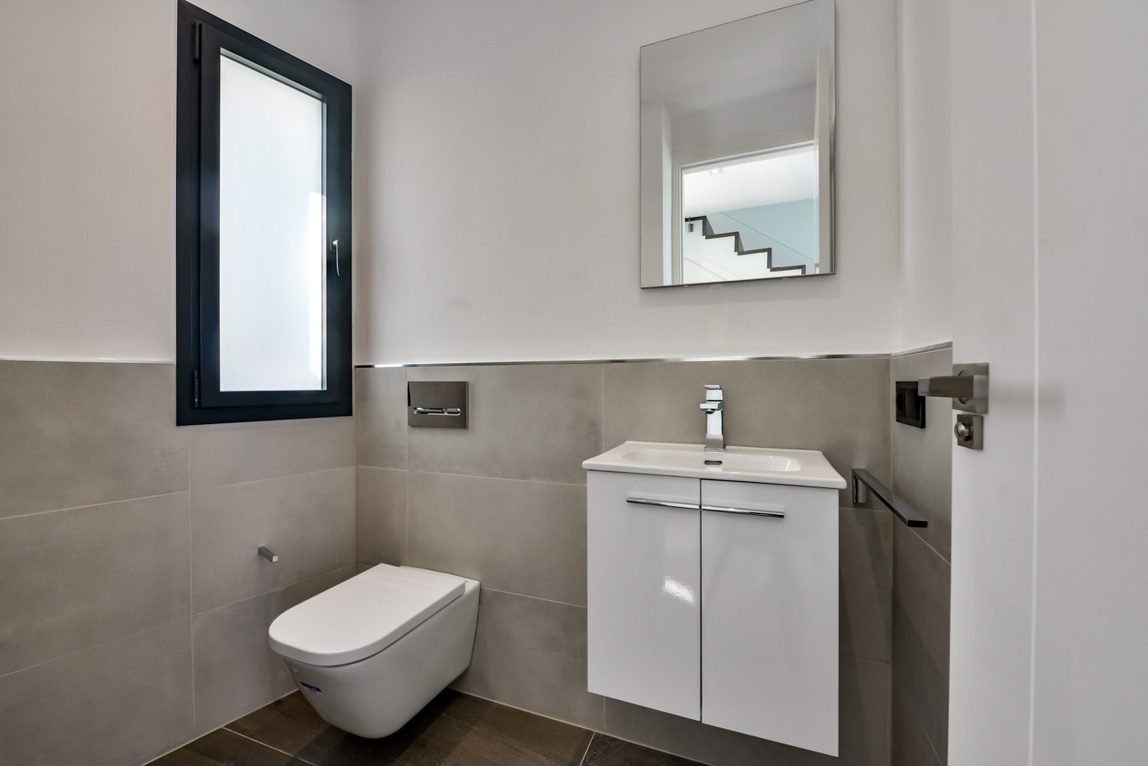 Toilettes invités avec WC suspendu, meuble vasque blanc minimaliste et fenêtre en verre dépoli avec cadre anthracite.