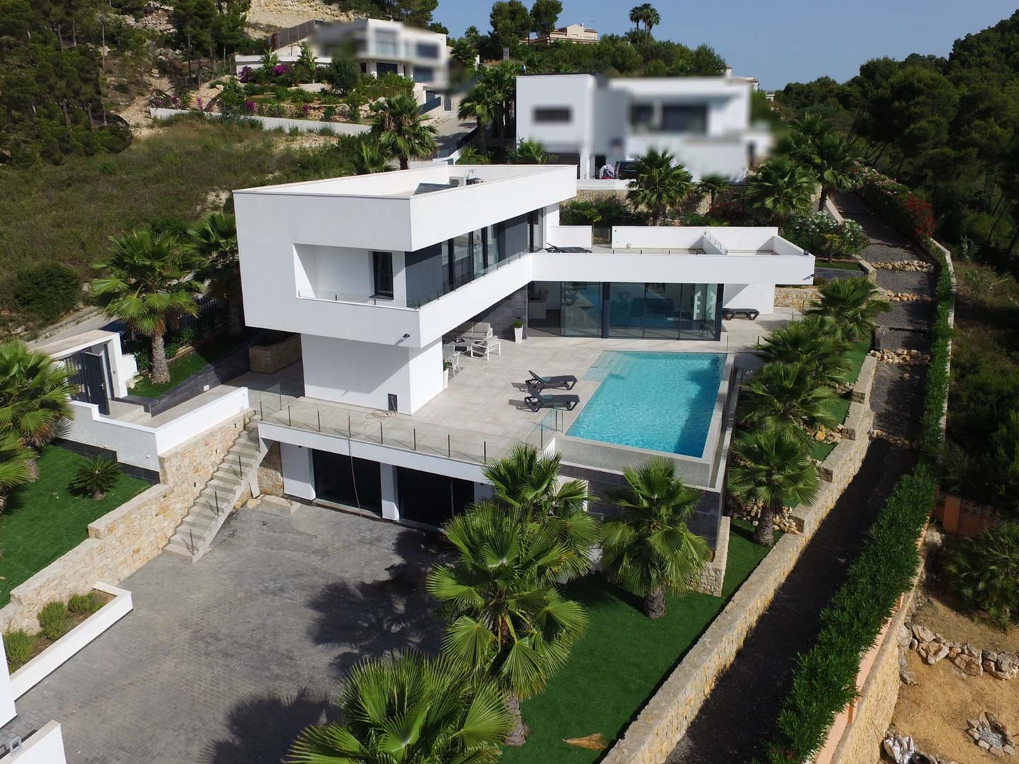 Vue aérienne de la villa moderne aux lignes épurées, avec piscine à débordement, terrasses en pierre et jardin méditerranéen planté de palmiers.