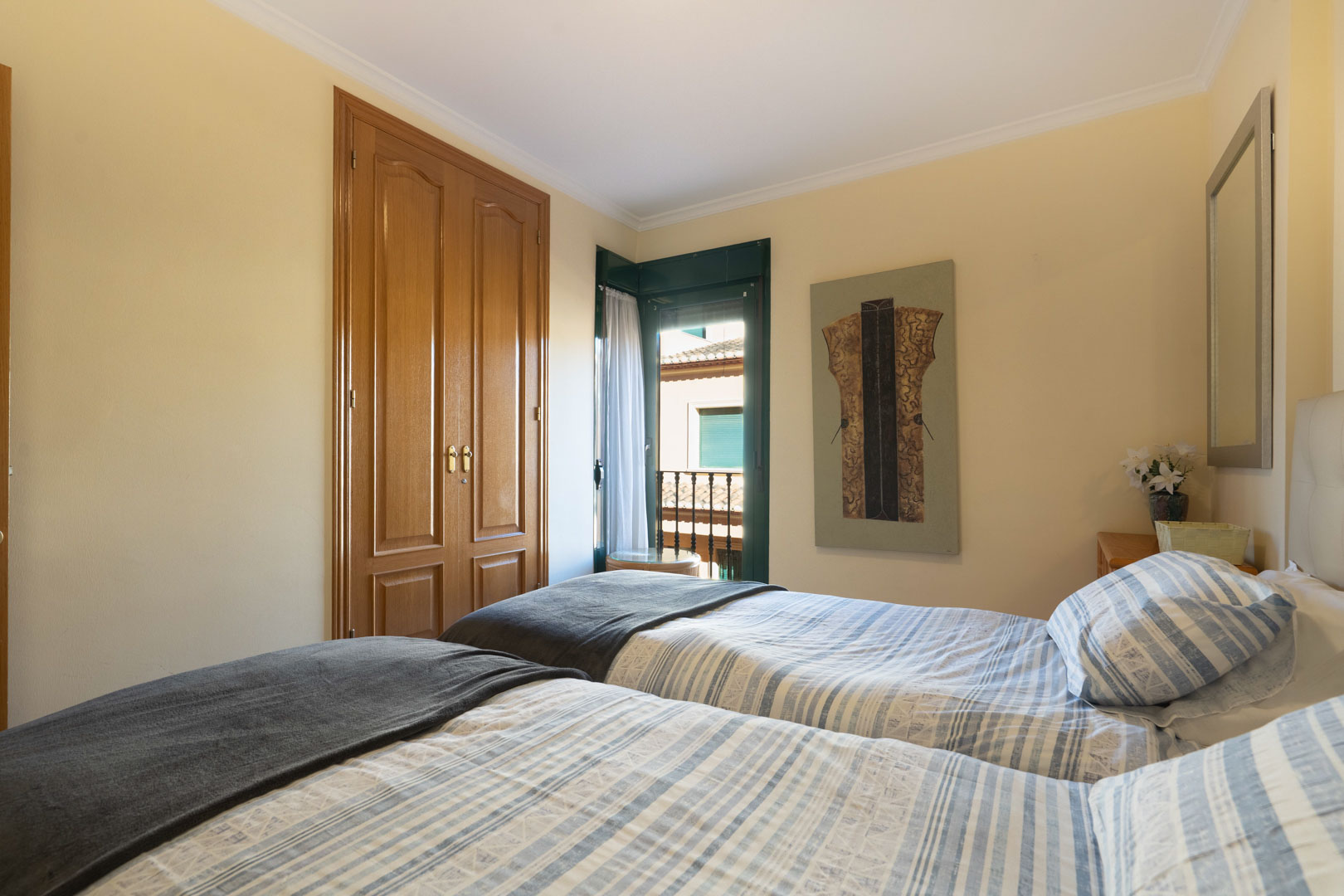 Chambre avec deux lits simples, une armoire encastrée en bois et un accès direct au balcon par une porte-fenêtre aux volets verts.