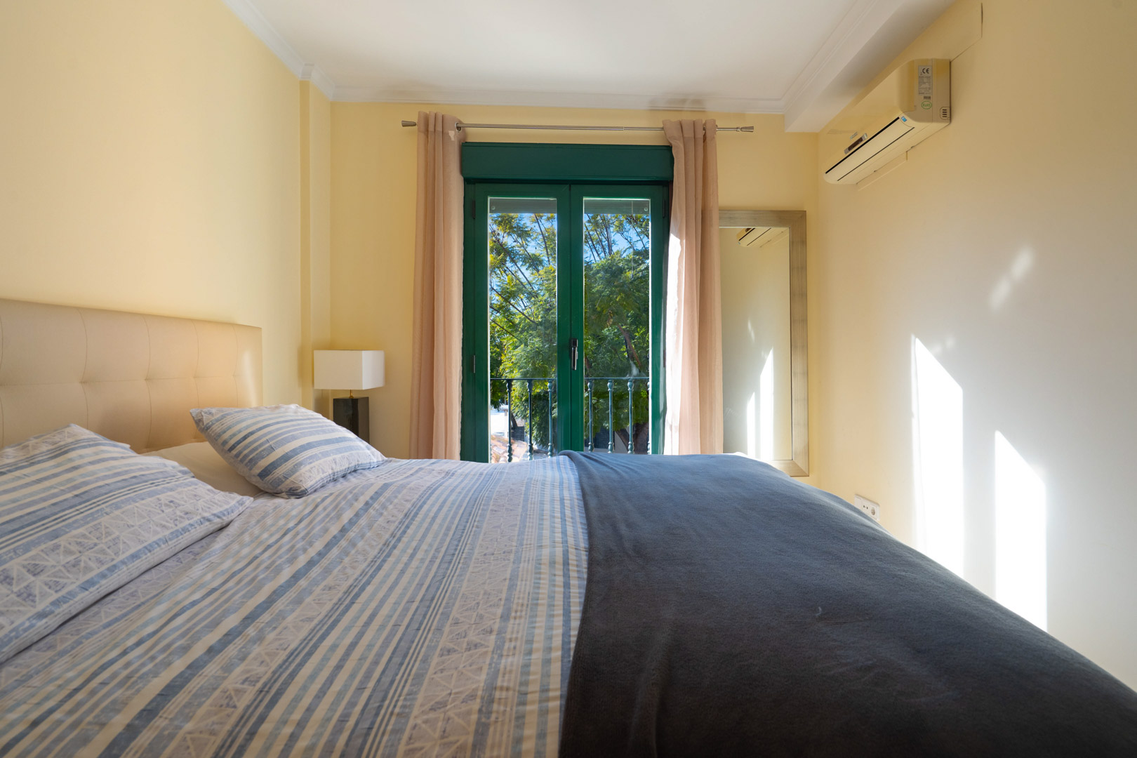 Chambre avec lit double, climatisation et portes-fenêtres vertes. La pièce bénéficie d'une lumière naturelle et d'une vue sur les jardins.