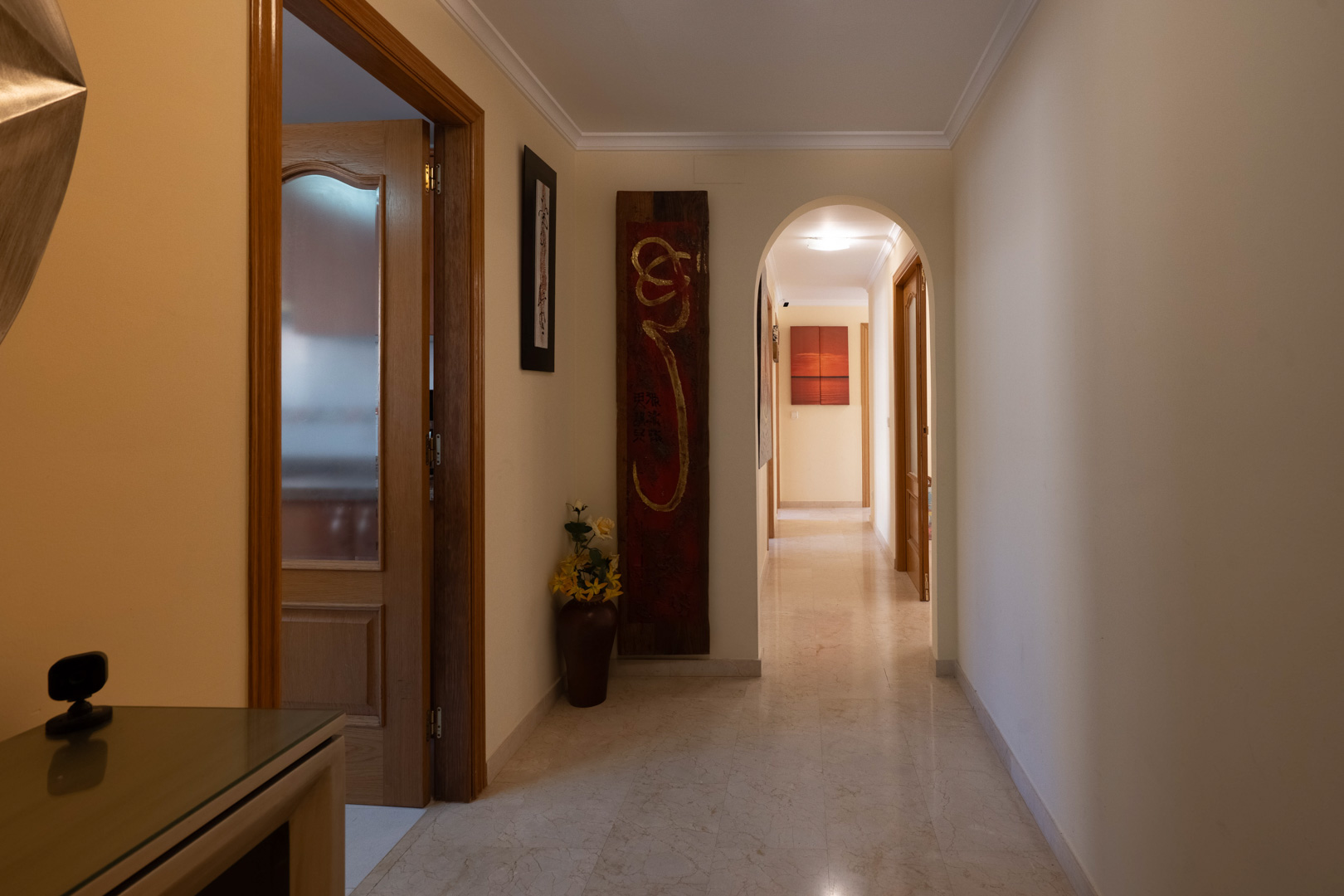 Couloir de distribution avec sol en marbre poli, moulures au plafond et une arche élégante menant aux chambres et pièces de vie.