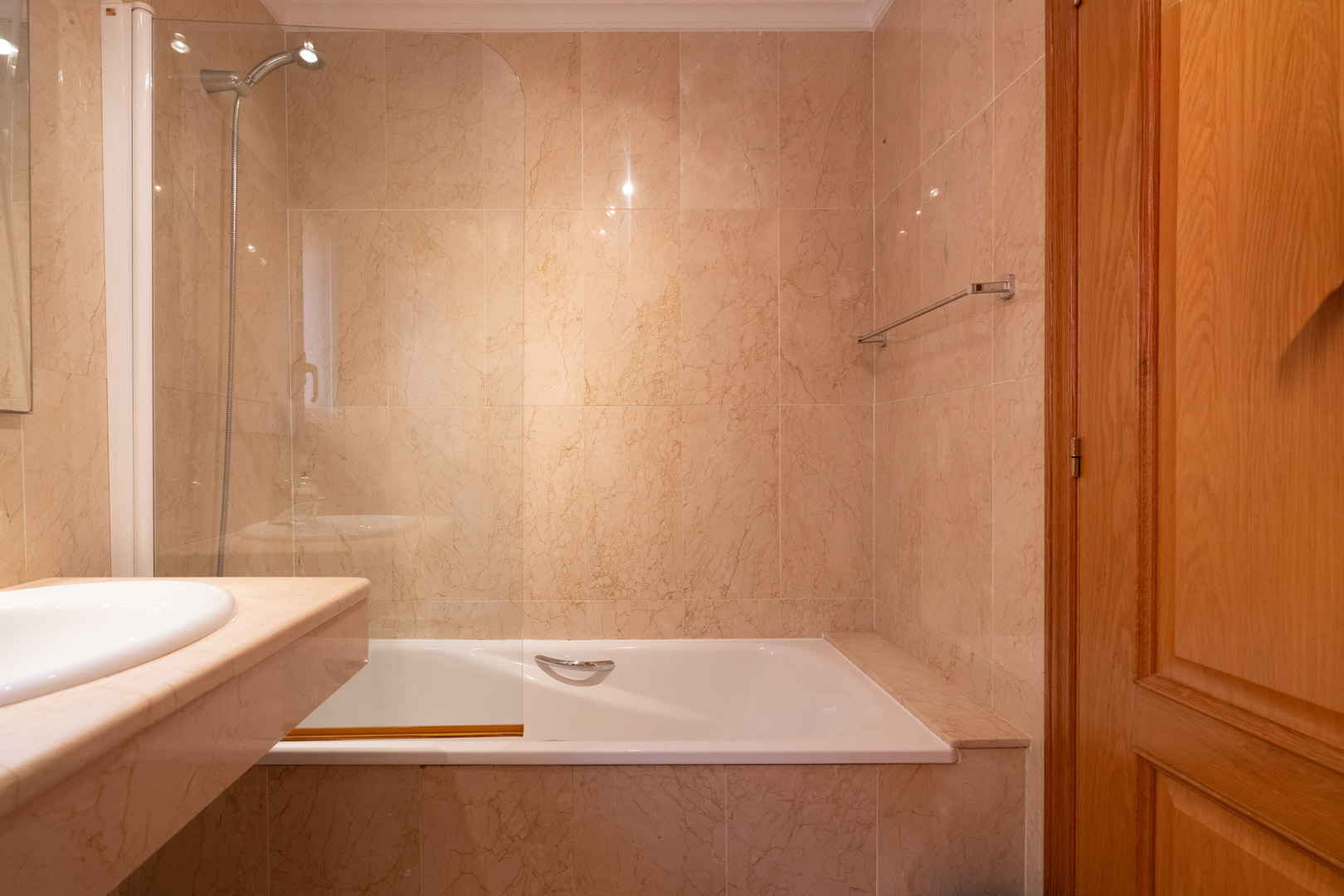 Salle de bain avec baignoire, paroi en verre et murs en marbre crème. Comprend un plan de vasque en pierre naturelle et une porte en bois massif.