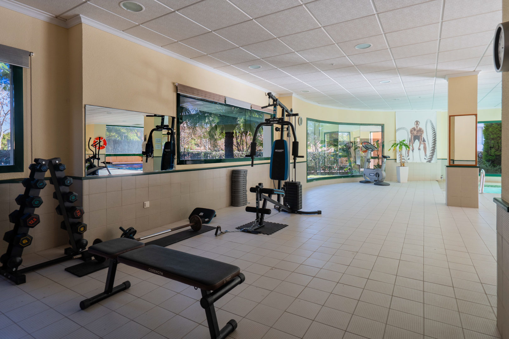 Salle de sport réservée aux résidents, équipée d'appareils de musculation et de cardio, bénéficiant d'une lumière naturelle abondante et de vues sur les jardins.