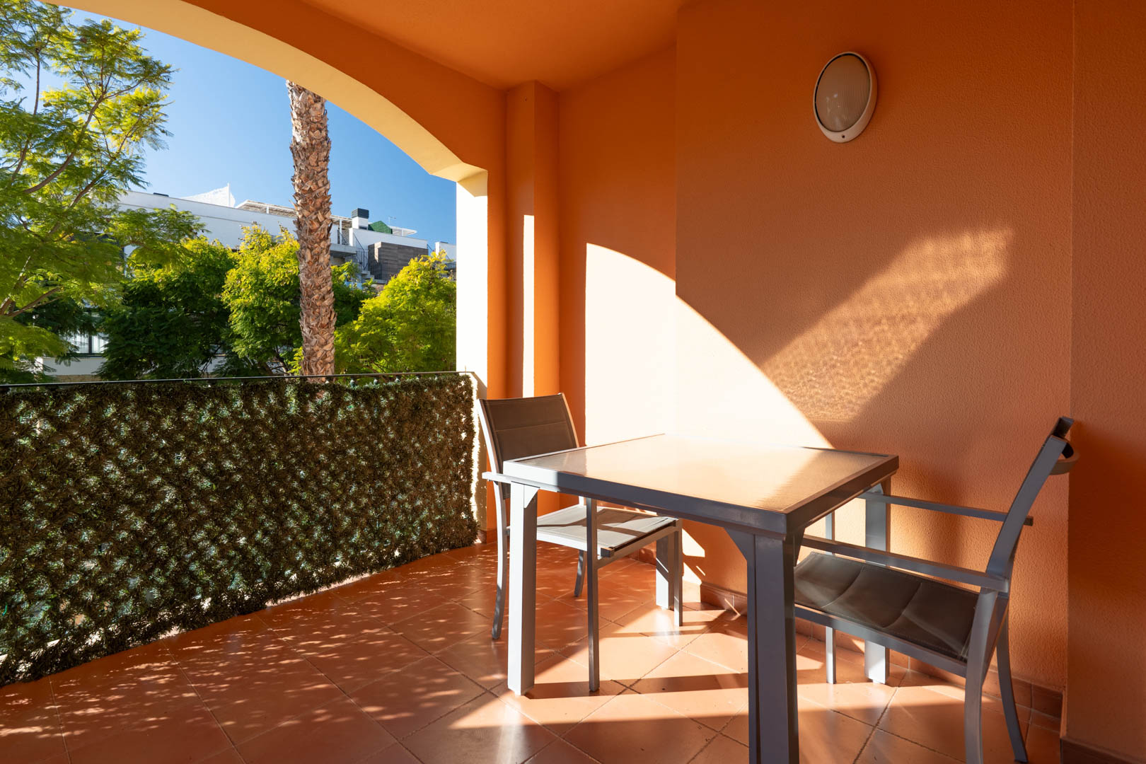 Terrasse couverte avec sol en terre cuite, mobilier d'extérieur moderne et vue sur la végétation luxuriante de la résidence.