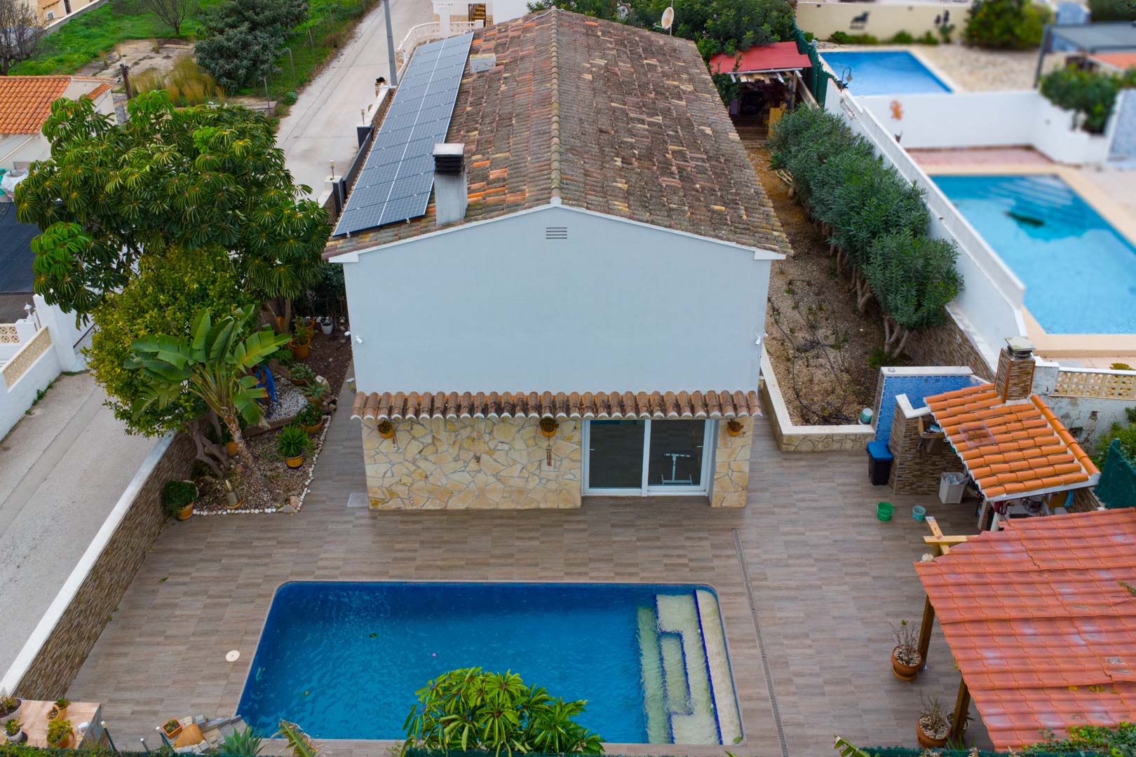 Vue aérienne de la villa avec panneaux solaires sur le toit, piscine privée et terrasse pavée comprenant une cuisine d'été couverte.