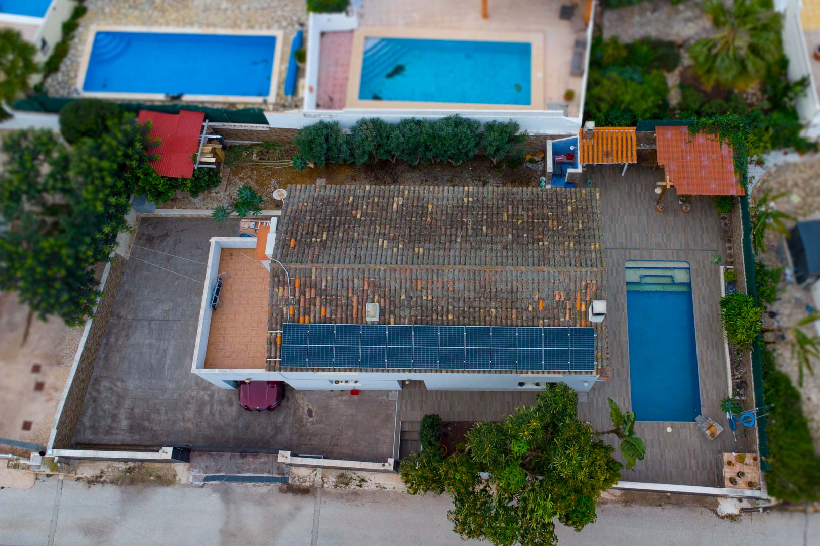 Vue aérienne de la villa illustrant les panneaux solaires sur le toit, la piscine rectangulaire et l'espace de stationnement pavé.