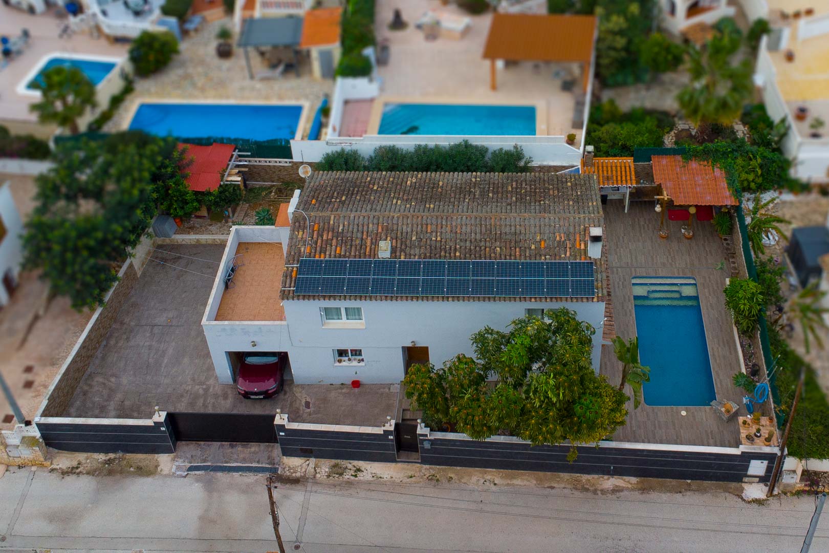 Vue aérienne de la villa mettant en évidence les panneaux solaires, la piscine privée avec terrasse et le garage intégré sur un terrain clos.