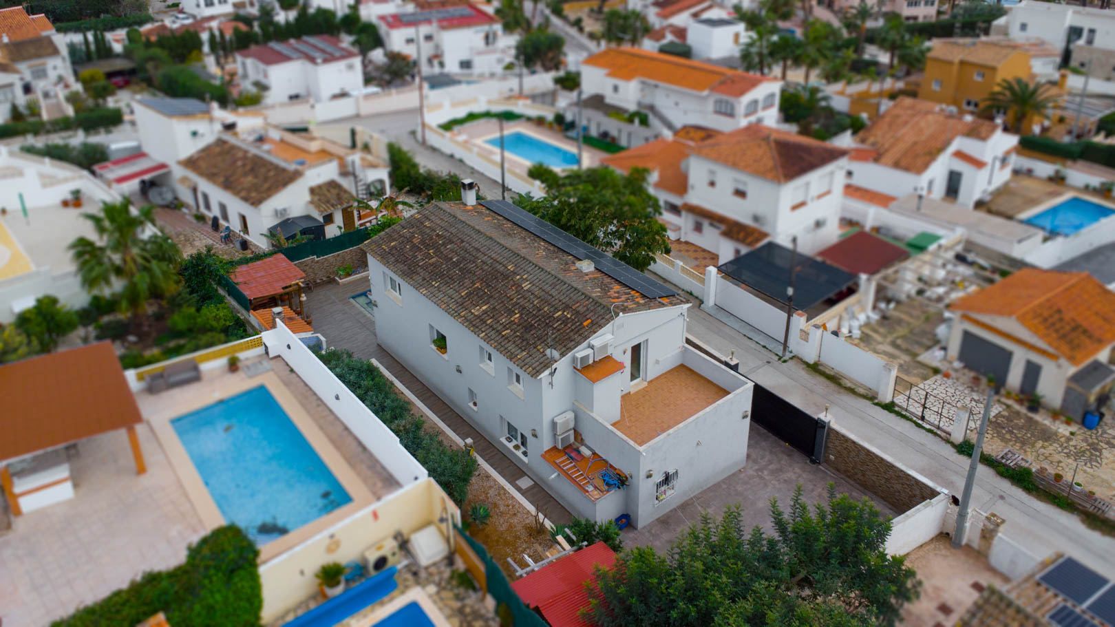 Vue aérienne de la villa montrant les panneaux solaires sur le toit, une terrasse à l'étage et l'aménagement extérieur dans un quartier résidentiel calme.